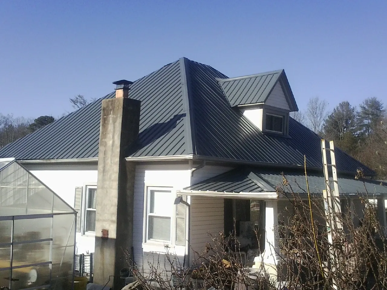 Dark blue standing seam metal roof on a white farmhouse with dormer — Slate & Tile Roof Repair by Roofing Brothers in Nekoma