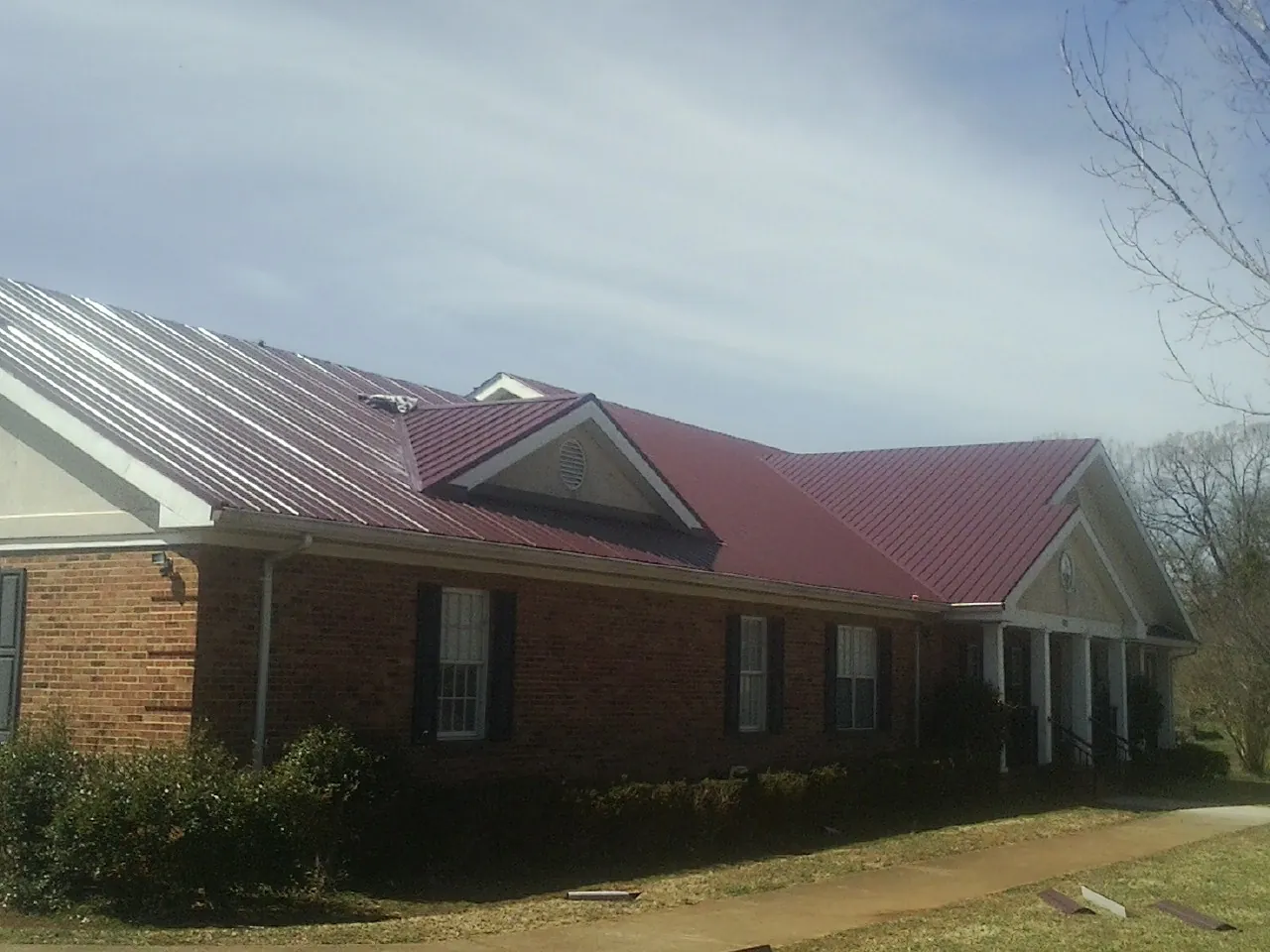 Red metal roof with gabled entries on a long brick building, from a Hail Damage Roof Repair job in Nekoma