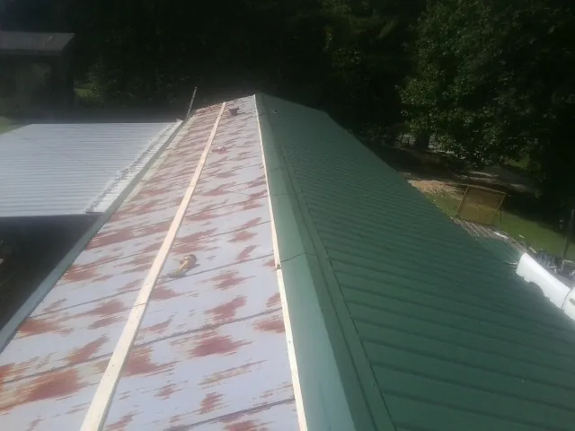Old rusted panels beside newly installed green metal roofing — Wind Damage Roof Repair by Roofing Brothers in Nekoma
