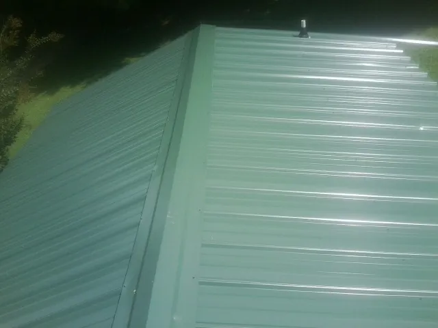New green metal panels meeting at the ridge of a roof — Flat Roof Repair work by our crew in Nekoma