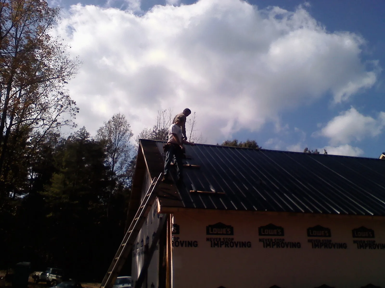 Roofer fastening dark metal panels high against a cloudy sky, from a Roof Inspection job in Nekoma