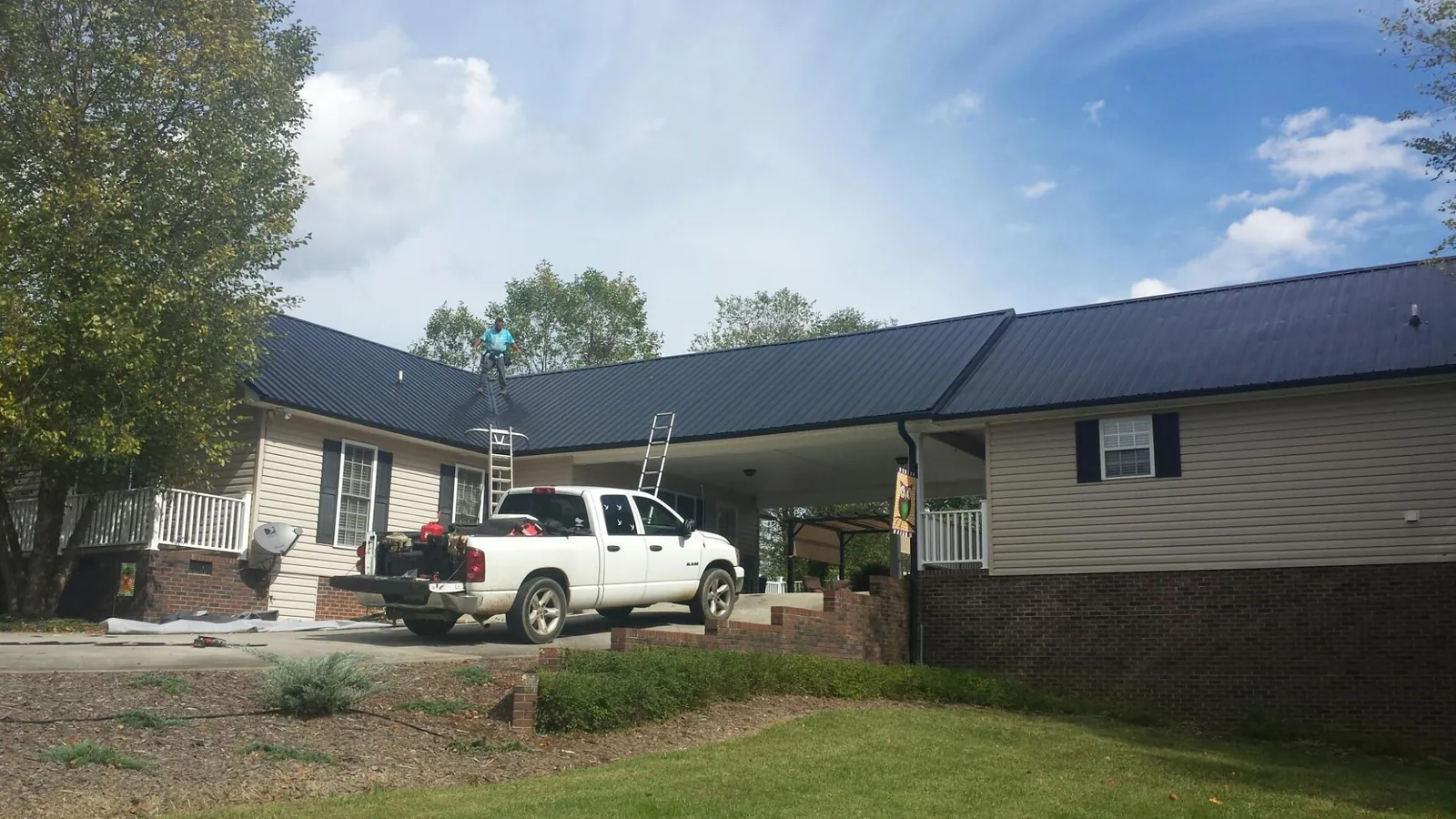 Black metal roof over a home and attached breezeway with ladders set in Nekoma