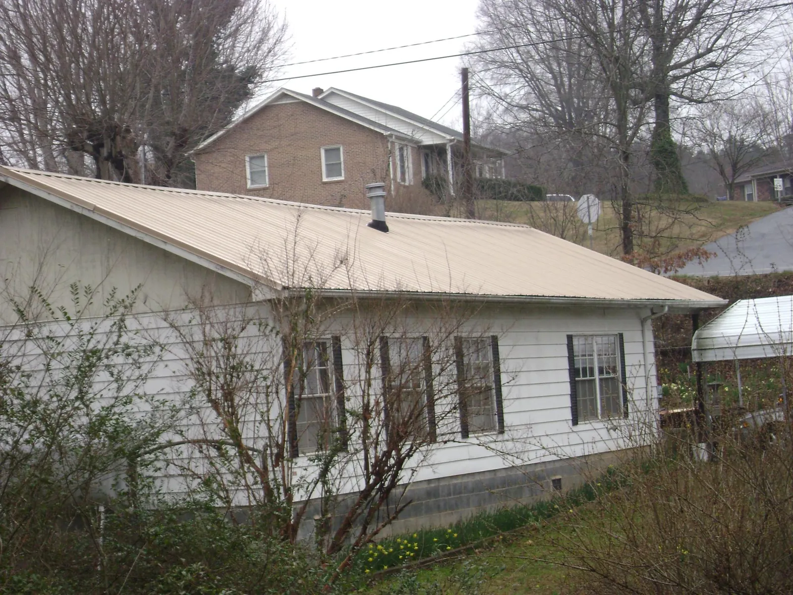 Tan metal roof on a white sided house set into a hillside — Commercial Roofing by Roofing Brothers in Nekoma
