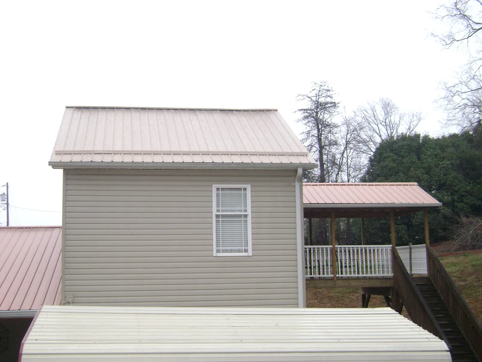 Tan metal roofs on a two story addition and attached porch, from a Roof Replacement job in Nekoma
